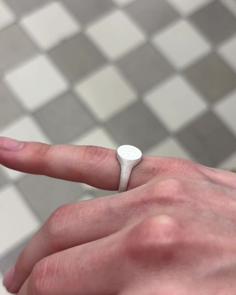 Chevalière en argent portée à l'index, plateau ovale gravé, au-dessus d'un sol en damier (image tirée du clip).