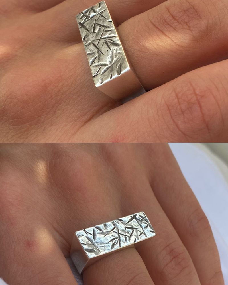 Deux vues de la bague portée, plateau rectangulaire poli à texture de traits en creux, sur tissu blanc.