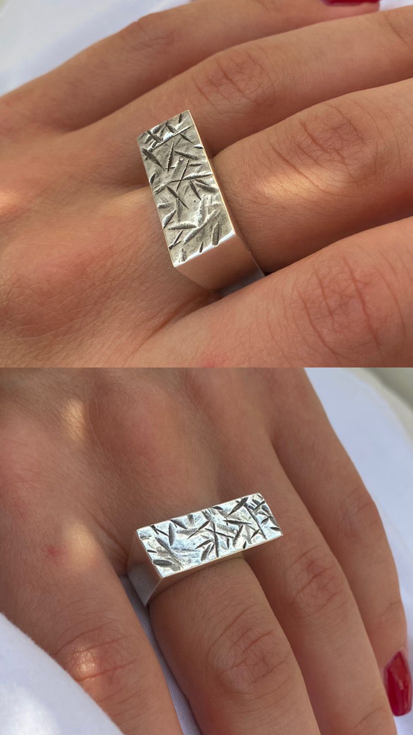 Deux vues de la bague portée, plateau rectangulaire poli à texture de traits en creux, sur tissu blanc.