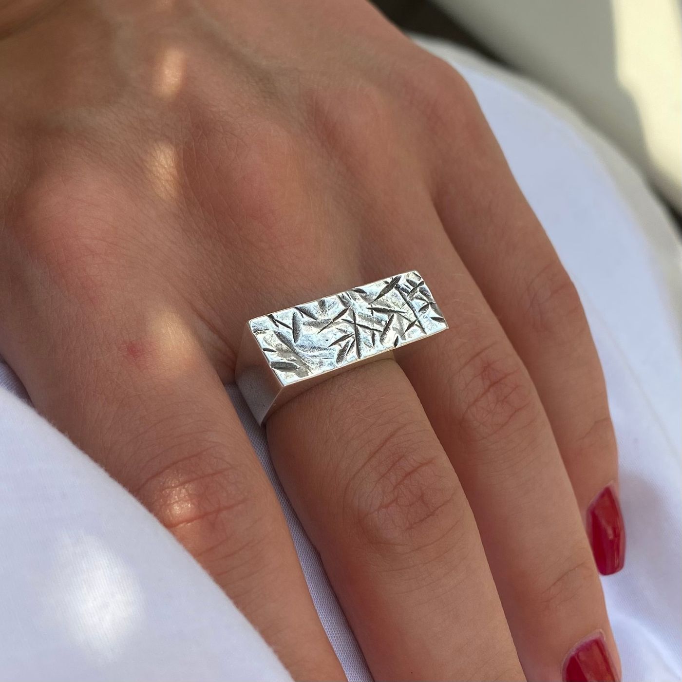 Bague portée, vue de trois quarts, plateau rectangulaire à traits en creux sur un anneau à pans droits.