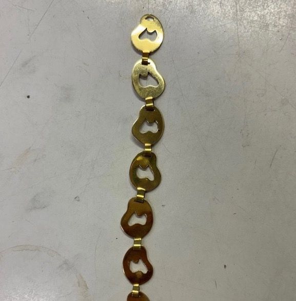 Bracelet à sept maillons plats en laiton posé à plat, chaque maillon ajouré d'un cœur, reliés par des languettes repliées.