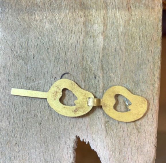 Deux maillons reliés par une languette repliée, posés sur une cheville d'établi en bois.