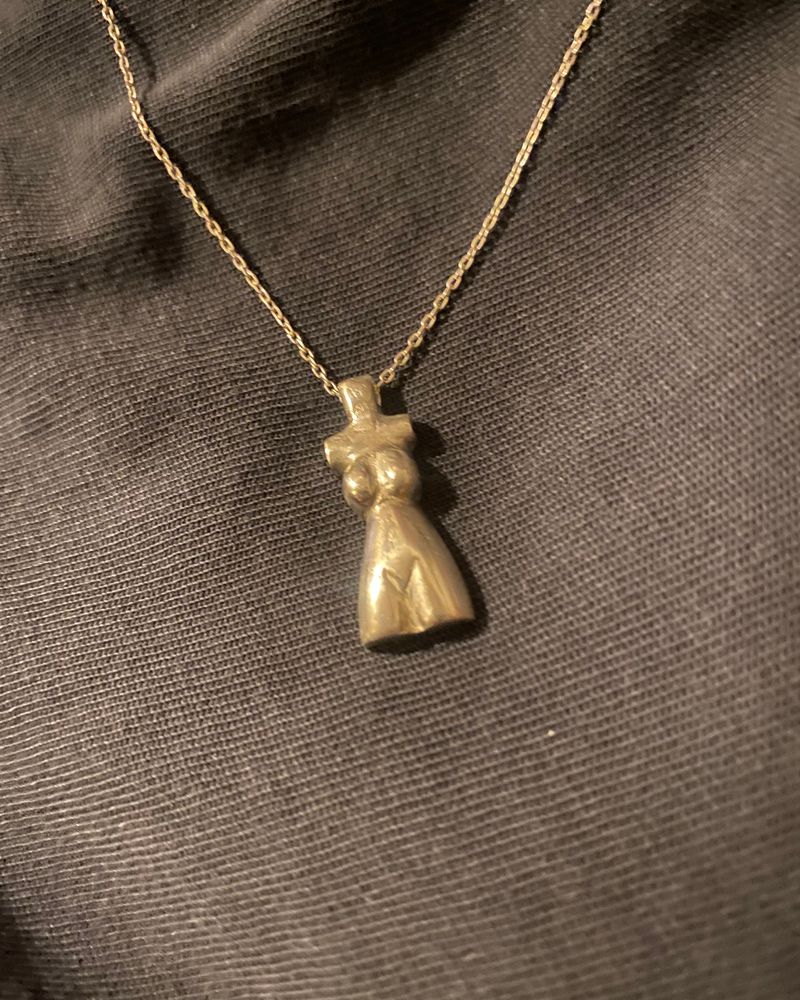 Pendentif en forme de torse féminin, coulé en argent et suspendu à une chaîne fine, sur tissu noir.
