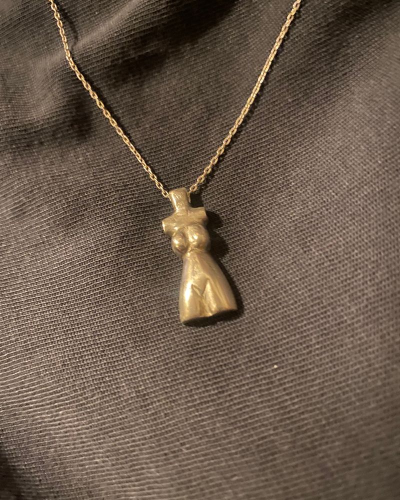 Pendentif en forme de torse féminin, coulé en argent et suspendu à une chaîne fine, sur tissu noir.