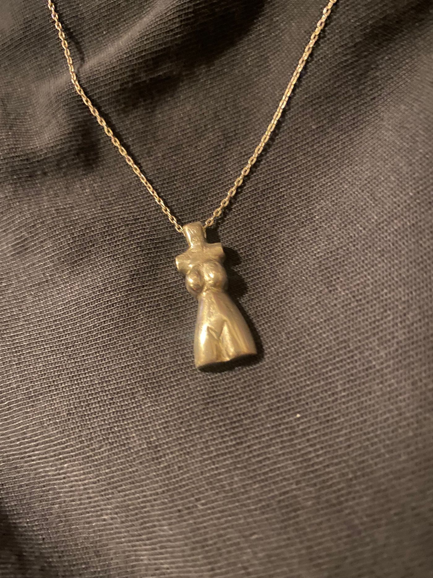 Pendentif en forme de torse féminin, coulé en argent et suspendu à une chaîne fine, sur tissu noir.